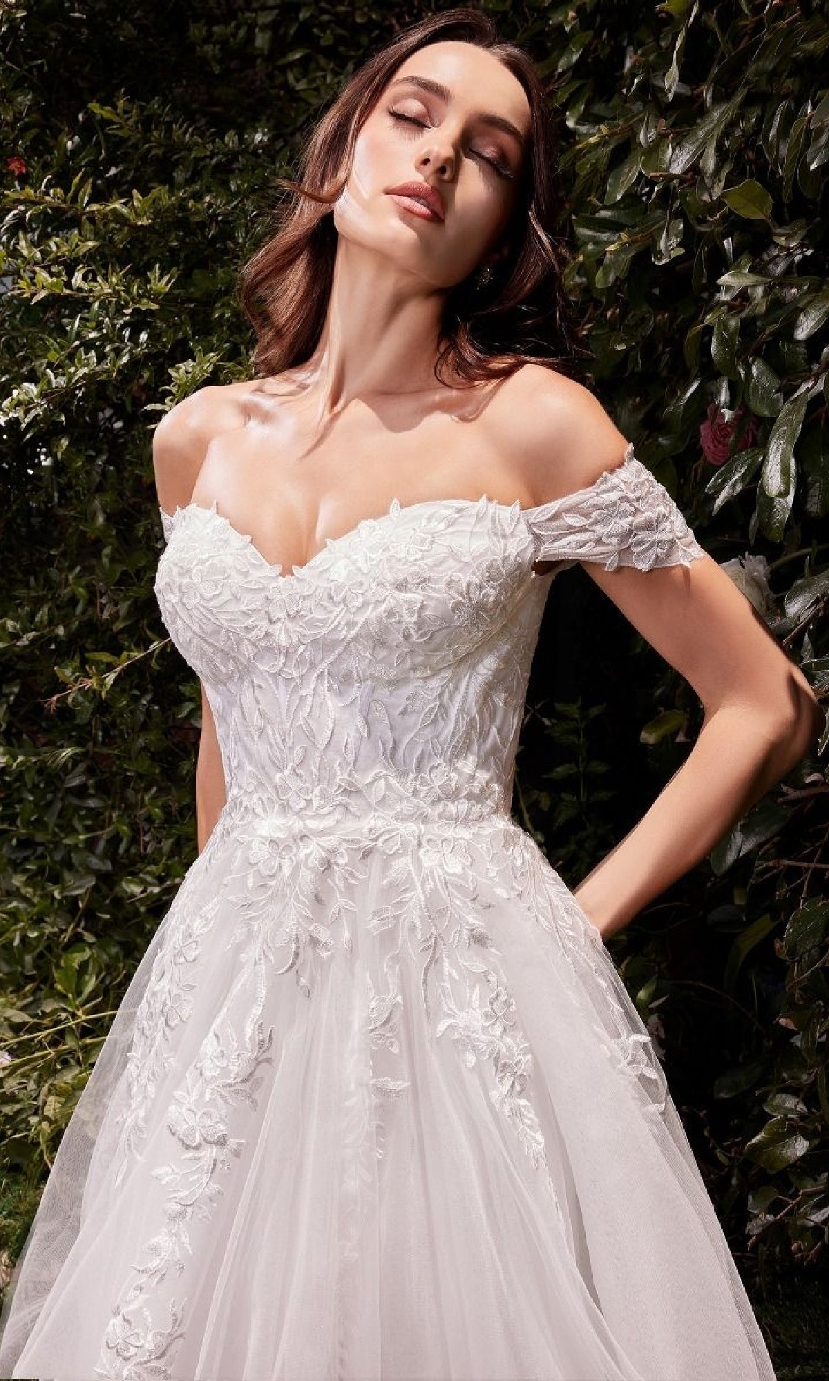 A woman stands outdoors among lush greenery, wearing the Ladivine C159W—an off-white, long wedding dress with off-the-shoulder lace.